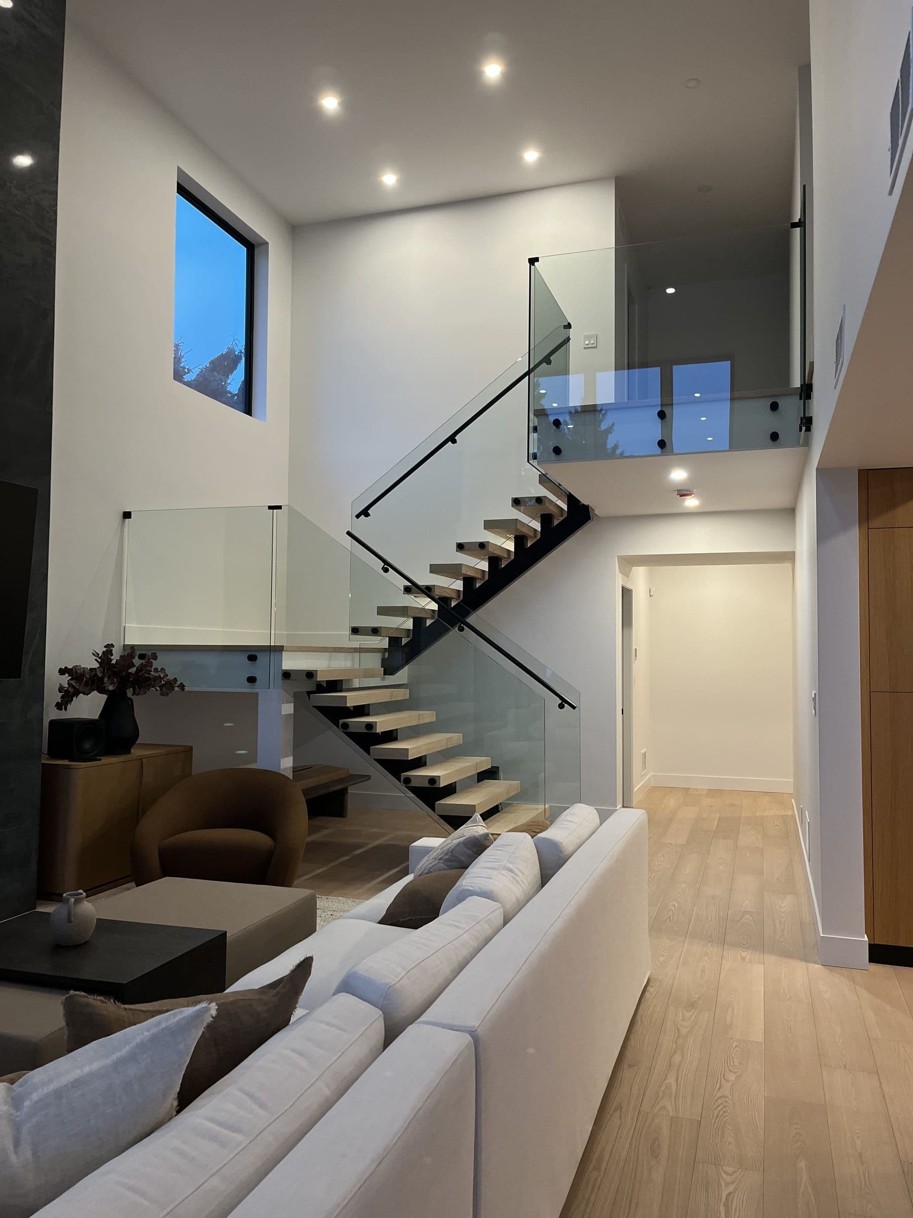 Frameless glass staircase railing and upper-landing balustrade in a modern open-concept living room