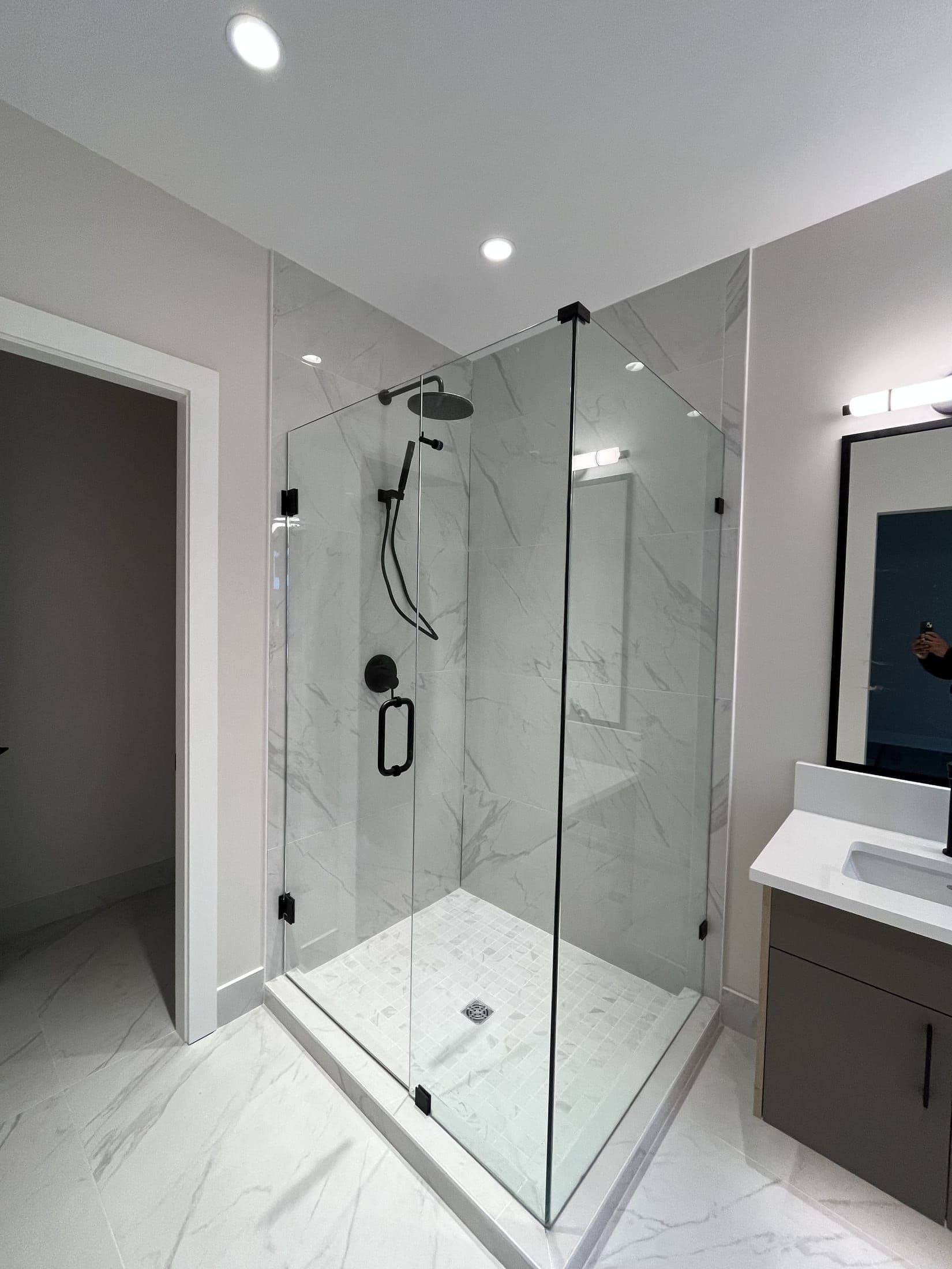 Frameless corner glass shower enclosure with matte black hardware and marble-look tile by Geet Glass & Closet
