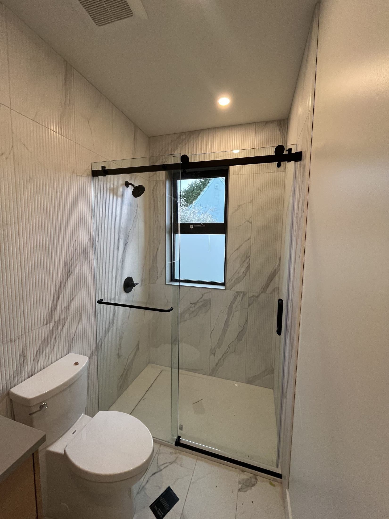Frameless sliding glass shower door with matte black barn-style hardware and marble-look tile