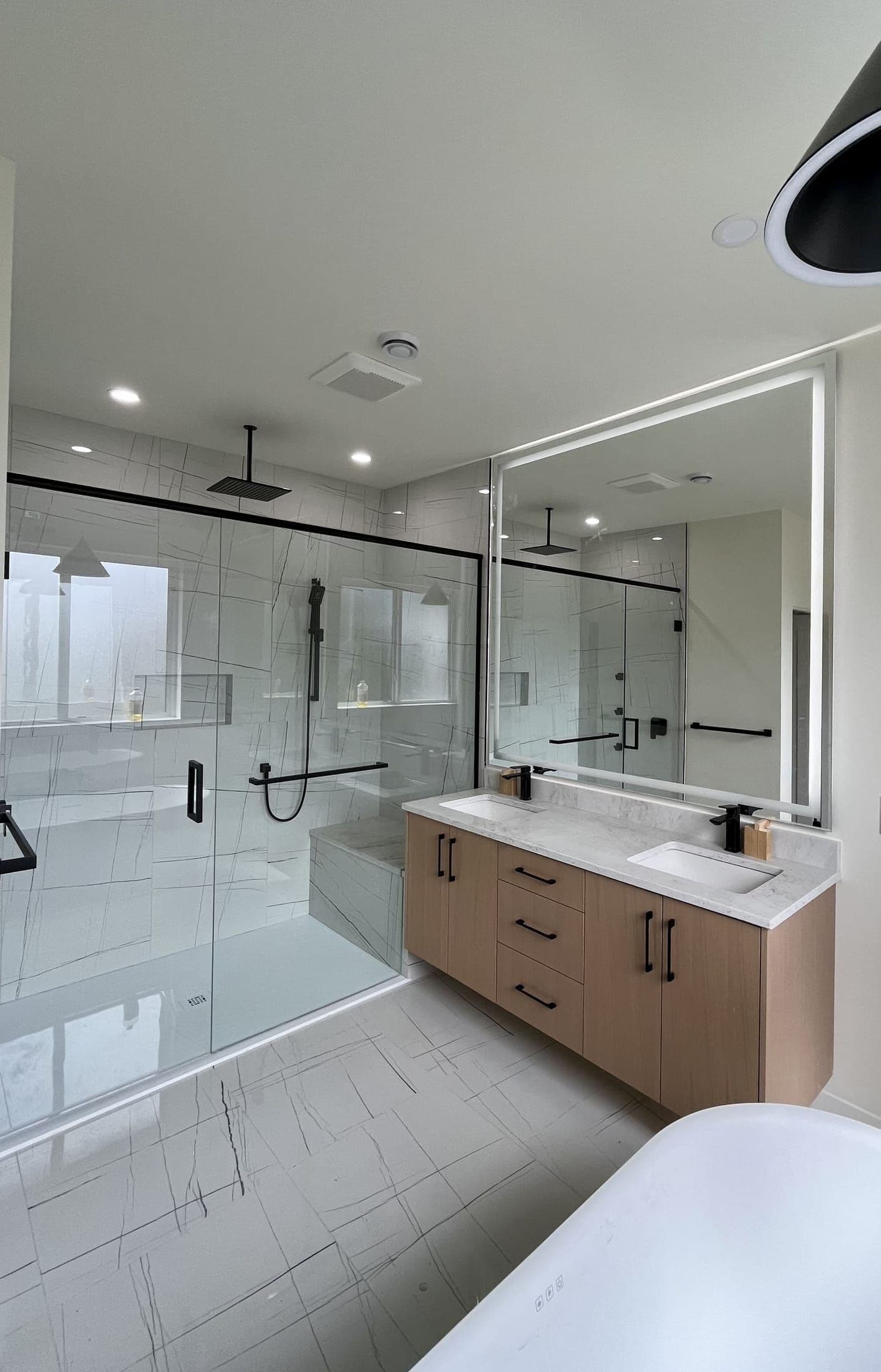 Black-framed glass shower enclosure and large LED vanity mirror in a modern master bathroom